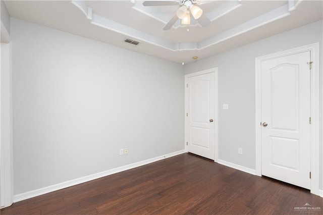 unfurnished bedroom featuring dark wood-type flooring, ceiling fan, and a tray ceiling