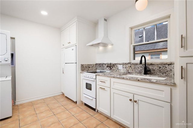 kitchen with white appliances, stacked washer and clothes dryer, wall chimney range hood, sink, and white cabinetry