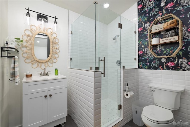 bathroom featuring vanity, toilet, a shower with door, and tile walls