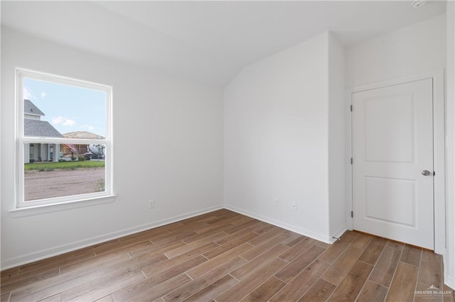 spare room with lofted ceiling, baseboards, and wood finished floors