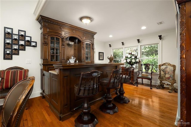 bar with dark brown cabinetry, hardwood / wood-style floors, and crown molding