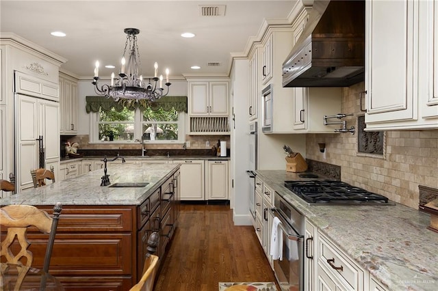 kitchen featuring premium range hood, sink, light stone counters, built in appliances, and pendant lighting