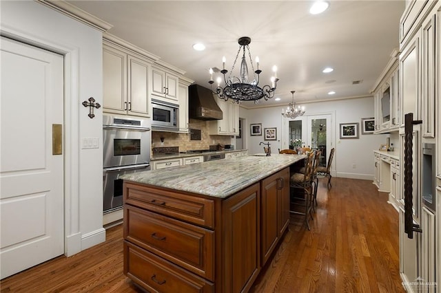 kitchen with tasteful backsplash, an island with sink, custom exhaust hood, hanging light fixtures, and stainless steel appliances