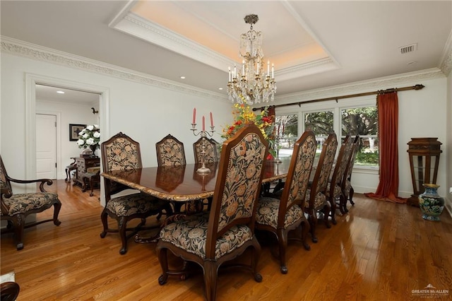 dining area with an inviting chandelier, ornamental molding, a tray ceiling, and hardwood / wood-style flooring