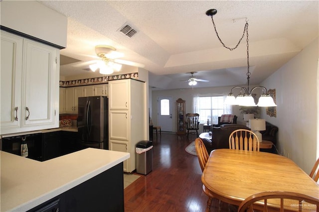 kitchen with ceiling fan with notable chandelier, pendant lighting, white cabinets, dark hardwood / wood-style flooring, and black fridge