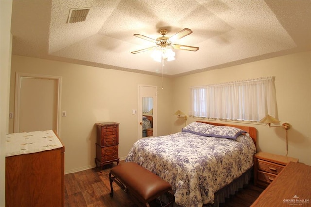 bedroom with ceiling fan, a tray ceiling, dark hardwood / wood-style floors, and a textured ceiling