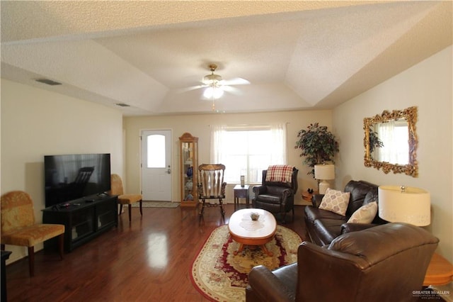 living room with ceiling fan, a textured ceiling, dark hardwood / wood-style flooring, and a tray ceiling