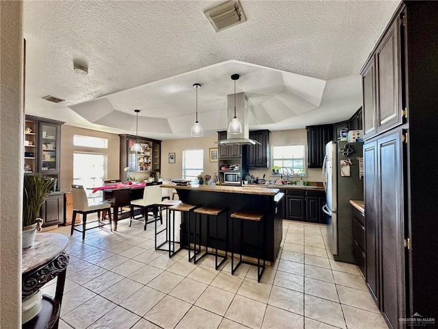 kitchen with a kitchen breakfast bar, a raised ceiling, light tile patterned floors, a kitchen island, and a textured ceiling