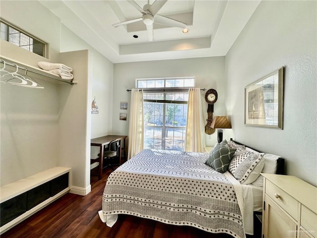 bedroom with ceiling fan, a tray ceiling, and dark wood-type flooring