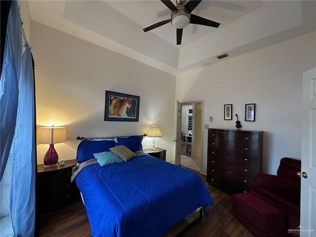 bedroom with ceiling fan, a tray ceiling, and dark hardwood / wood-style flooring