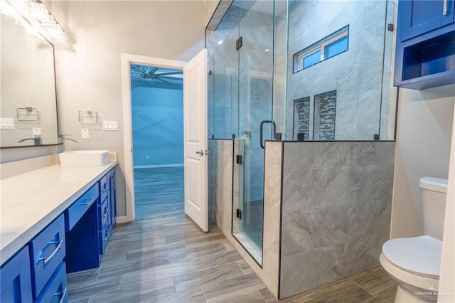 bathroom featuring a shower with door, vanity, ceiling fan, and toilet