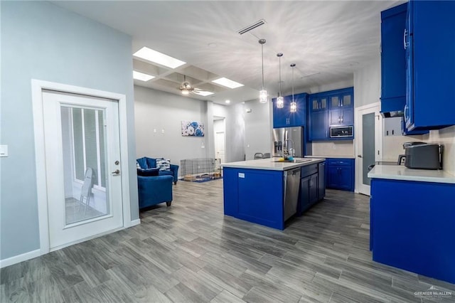 kitchen featuring a skylight, hardwood / wood-style floors, pendant lighting, stainless steel appliances, and a kitchen island with sink