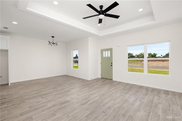 unfurnished living room with ceiling fan with notable chandelier, light hardwood / wood-style floors, and a wealth of natural light