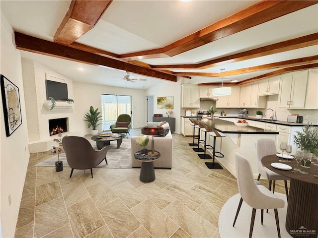 living room featuring ceiling fan, a large fireplace, lofted ceiling with beams, and sink