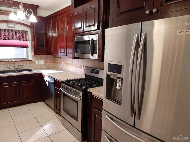 kitchen featuring appliances with stainless steel finishes, hanging light fixtures, a sink, light countertops, and backsplash