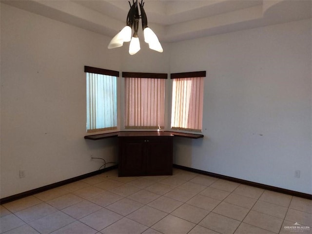 empty room featuring light tile patterned floors, built in desk, a raised ceiling, and baseboards