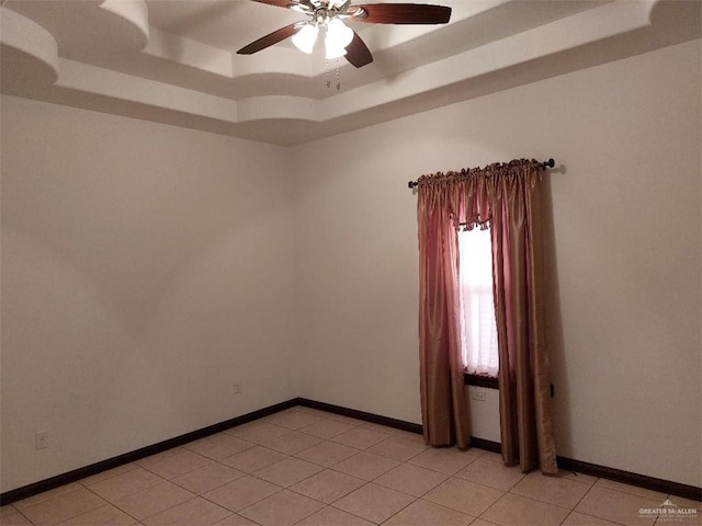 empty room featuring a tray ceiling, ceiling fan, baseboards, and light tile patterned floors