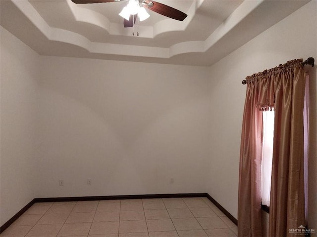 spare room with a raised ceiling, light tile patterned flooring, and baseboards