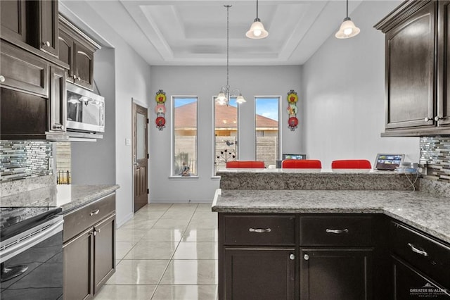 kitchen featuring decorative light fixtures, dark brown cabinetry, stainless steel appliances, and a tray ceiling