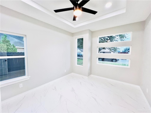 spare room with ceiling fan, a healthy amount of sunlight, and a tray ceiling