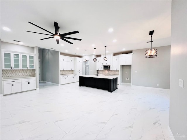 kitchen with backsplash, decorative light fixtures, and a kitchen island with sink