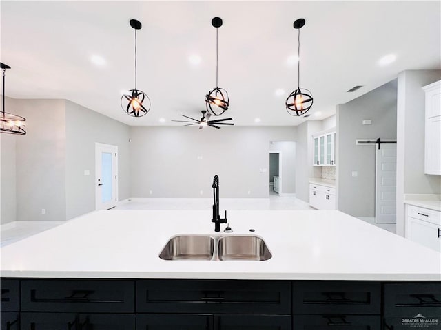 kitchen featuring white cabinets, sink, a barn door, an island with sink, and decorative light fixtures