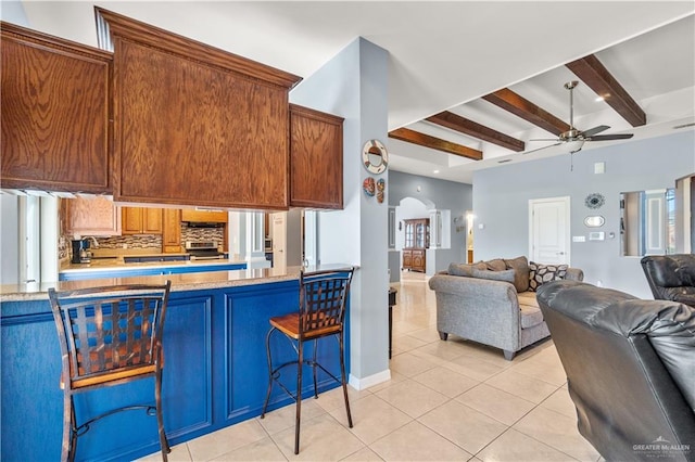 705 W Vinson Ave, Harlingen, TX 78550 - kitchen featuring light tile patterned floors, ceiling fan, backsplash, a kitchen bar, and beamed ceiling