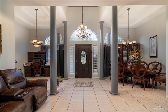 tiled entryway with a tray ceiling, a chandelier, and ornate columns