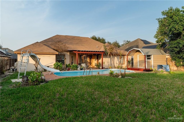 rear view of property with a fenced in pool, a yard, a patio, and a storage unit