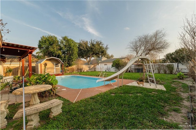 view of pool featuring a lawn, a storage unit, and a water slide