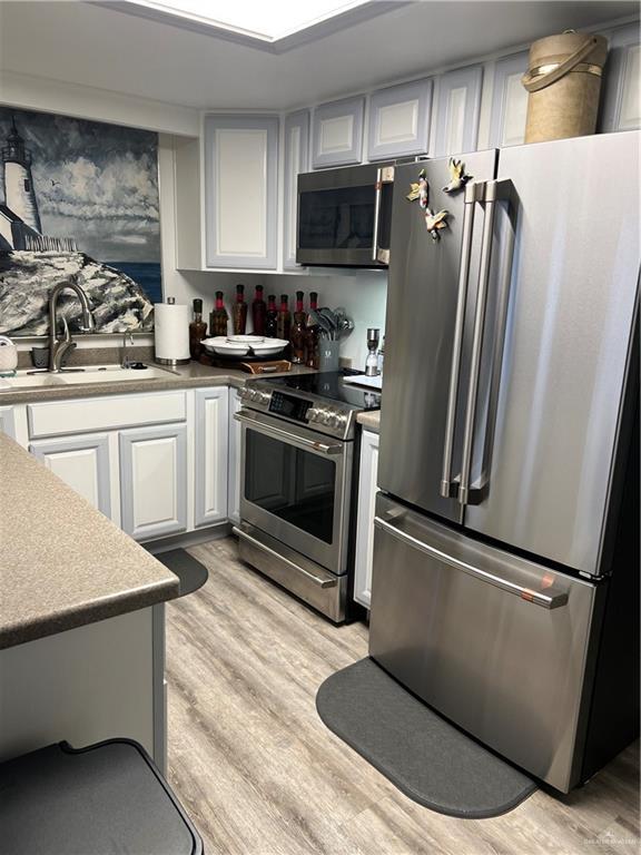 kitchen featuring stainless steel appliances, light wood-type flooring, white cabinets, and a sink