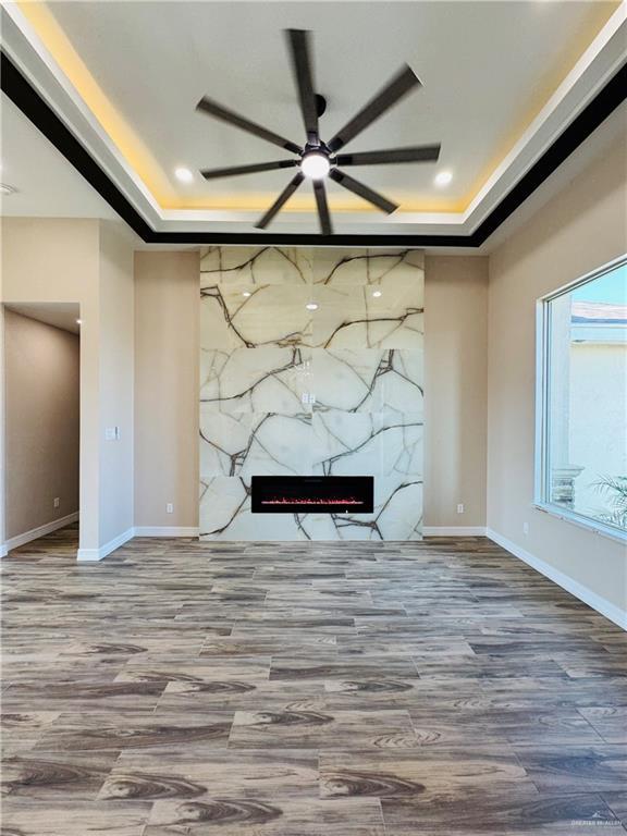 unfurnished living room featuring a premium fireplace, hardwood / wood-style floors, ceiling fan, and a tray ceiling