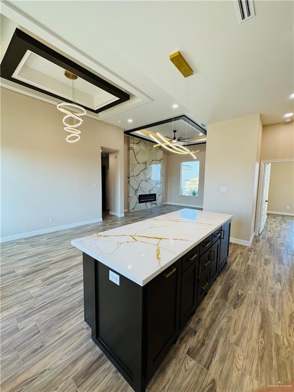 kitchen with a fireplace, decorative light fixtures, light hardwood / wood-style floors, a tray ceiling, and light stone counters