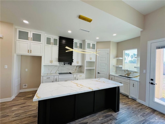 kitchen with sink, light stone countertops, a center island, and white cabinets