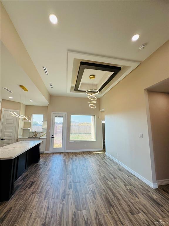 unfurnished living room with a tray ceiling, dark hardwood / wood-style floors, and a chandelier