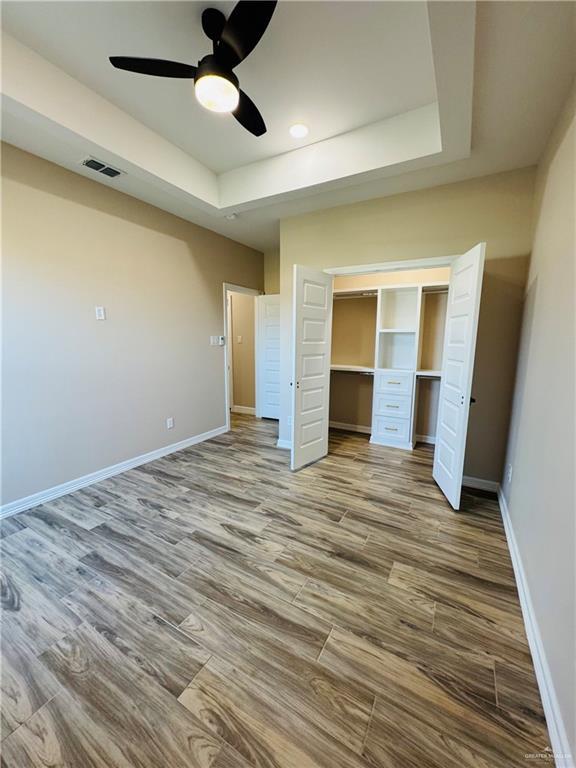 unfurnished bedroom with hardwood / wood-style flooring, ceiling fan, a tray ceiling, and a closet