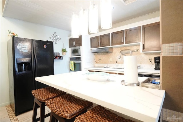 6608 Padre Blvd, South Padre Island, TX 78597 - kitchen featuring stainless steel appliances, under cabinet range hood, dark brown cabinets, tasteful backsplash, and a breakfast bar area