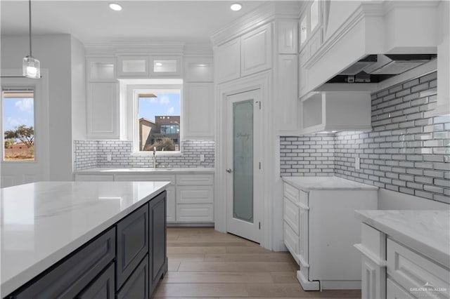 kitchen featuring custom exhaust hood, backsplash, white cabinets, and decorative light fixtures