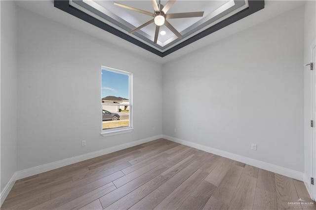 unfurnished room featuring ceiling fan, light wood-type flooring, and a raised ceiling