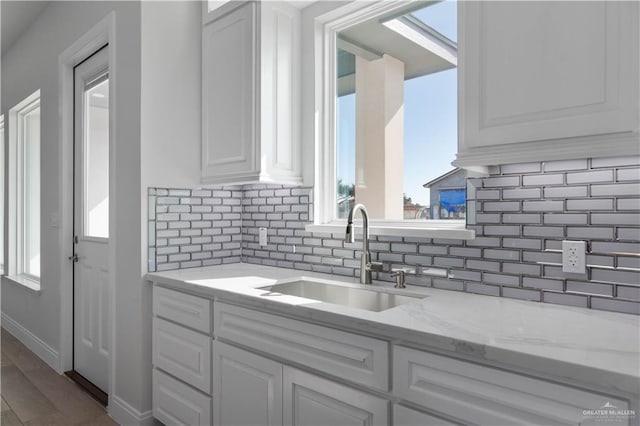 kitchen with sink, light stone counters, white cabinetry, and hardwood / wood-style flooring