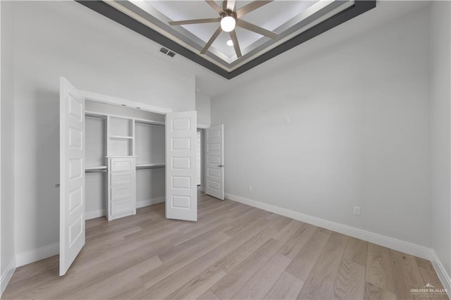 unfurnished bedroom featuring ceiling fan, a closet, a tray ceiling, and light hardwood / wood-style floors