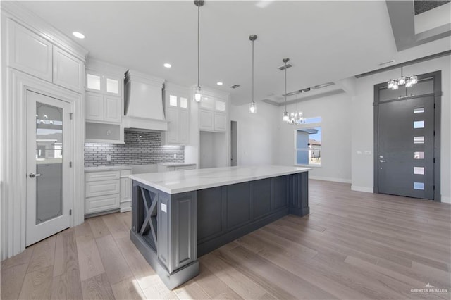 kitchen with white cabinetry, decorative light fixtures, a spacious island, and custom range hood