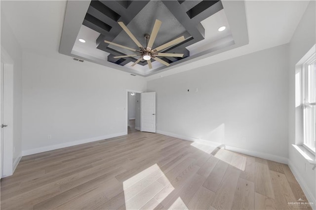 empty room with light wood-type flooring, ceiling fan, a raised ceiling, and coffered ceiling