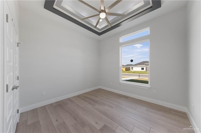 unfurnished room featuring ceiling fan, light hardwood / wood-style flooring, and a tray ceiling