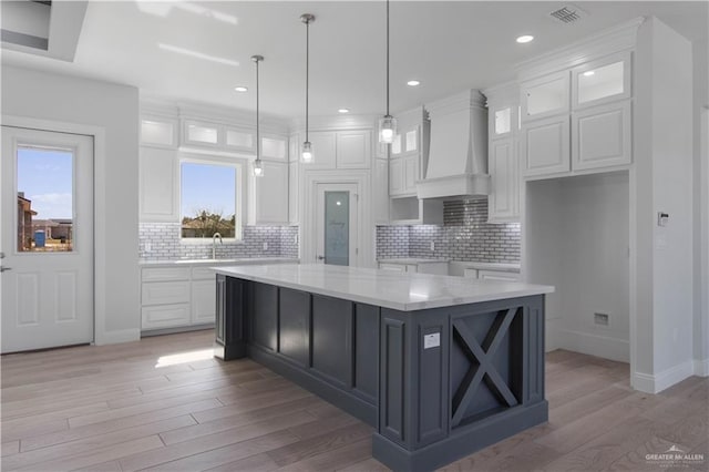 kitchen with custom exhaust hood, hanging light fixtures, light stone countertops, a kitchen island, and white cabinets