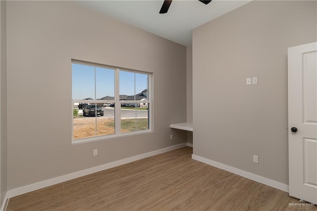 empty room featuring baseboards, light wood finished floors, and ceiling fan