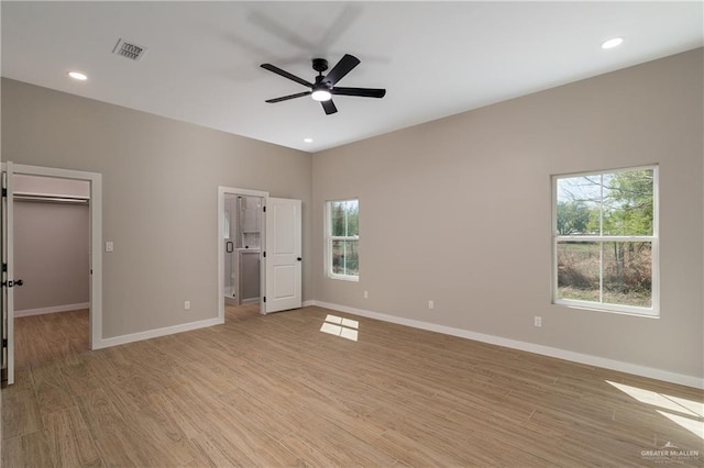 unfurnished bedroom featuring a spacious closet, multiple windows, light wood-style floors, and baseboards