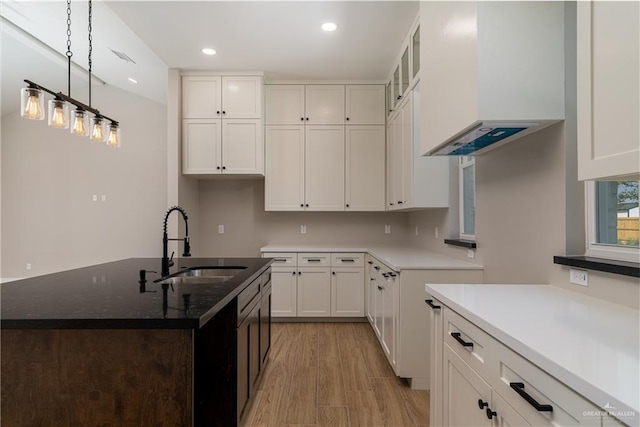 kitchen featuring dark stone countertops, a sink, hanging light fixtures, white cabinets, and light wood-type flooring