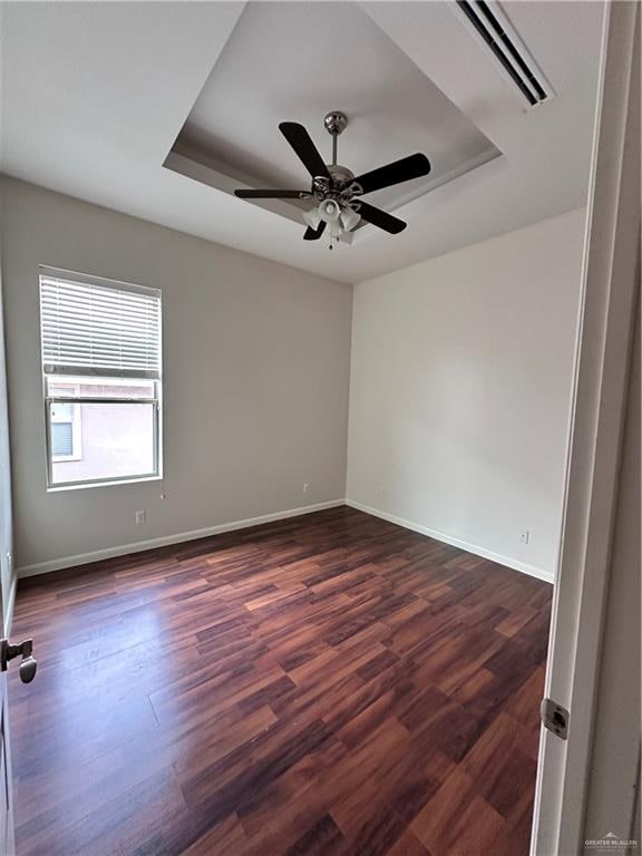 spare room with ceiling fan, dark wood-type flooring, and a tray ceiling