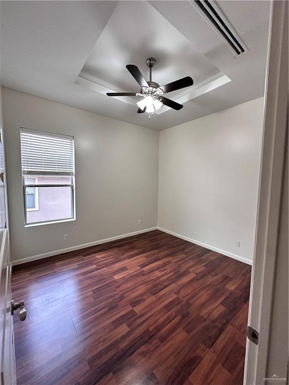 empty room with ceiling fan, dark hardwood / wood-style flooring, and a tray ceiling